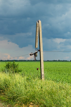 Damaged concrete power line pole with broken wires with storm clouds in the sky on a summer dayの写真素材