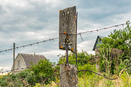 Old concrete pillar and barbed wire fence in a rural area with houses in the background blurred. Soft Selective Focusの写真素材
