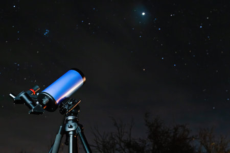 An astronomical telescope on a tripod is ready for stargazing at night. A modern optical device for studying starry sky objectsの写真素材
