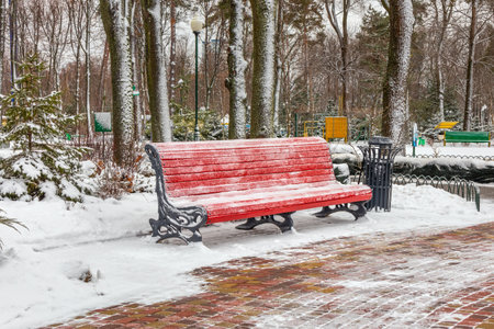 Large empty bench in a city park or garden on a winter day. Red wooden bench and metal urnの写真素材