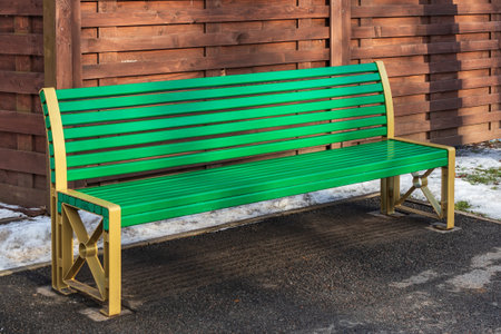 Modern green bench in a park on the asphalt near a wooden fenceの写真素材