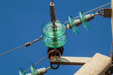 Glass insulators and wires of a high-voltage overhead power line against a background of blue sky on...