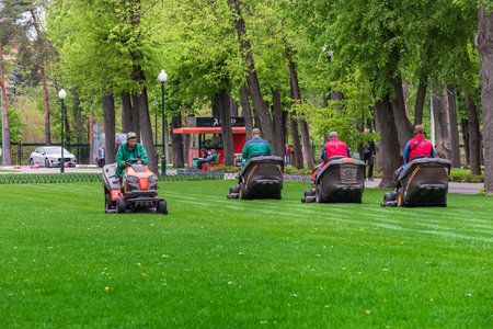 Kharkiv city, Ukraine - April 18, 2024: Mowing the lawn in a city park. Male workers at tractor lawn mowerのeditorial素材