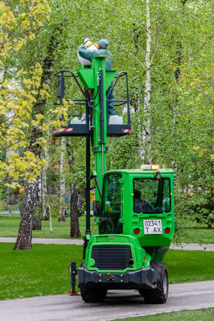 Kharkiv city, Ukraine - April 18, 2024: A utility worker cleans a street lamp on a green aerial platform in a park on an alleyのeditorial素材