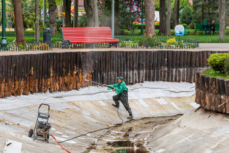 Kharkiv city, Ukraine - April 18, 2024: A male worker cleans the bottom of a pond using a high-pressure washer in a city park. Spring pond cleaning workのeditorial素材