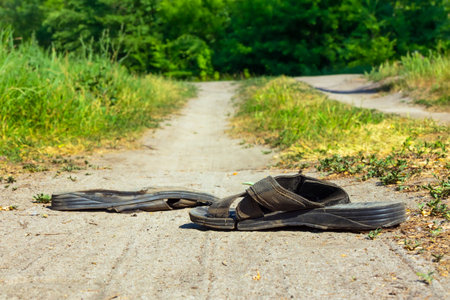 Black torn slippers on a dusty road. Abandoned shoes on a country road. Sunny summer day, no peopleの写真素材