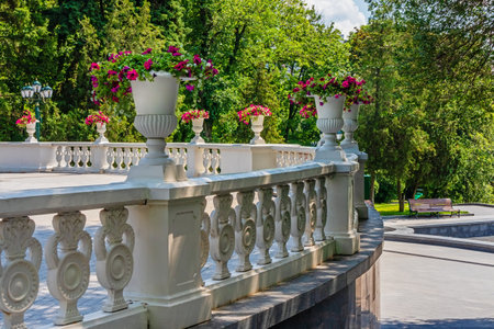 Old vintage vases with flowers and a stone white decorative fence on a cascade in the city garden of Kharkiv city, Ukraine. Picturesque retro park on a sunny summer dayの写真素材