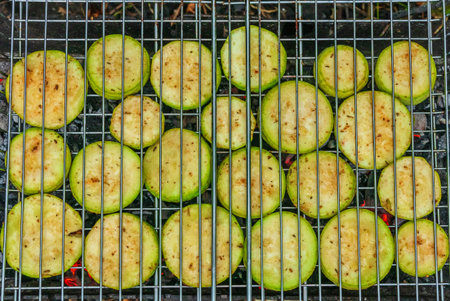 Sliced zucchini pieces are grilled in a metal grate. Vegetarian food - vegetables are cooked over hot coalsの写真素材
