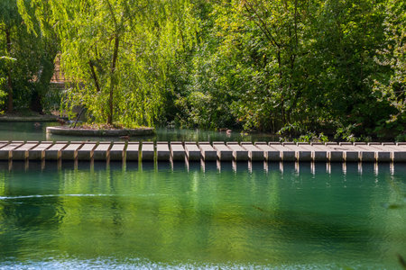 Modern concrete pedestrian bridge on a pond in a city garden or park on a sunny summer day. Modern architecture in garden designの写真素材