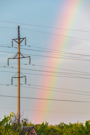 Rainbow in the sky and high-voltage power line with wires and concrete pole. Electric power transmissionの写真素材
