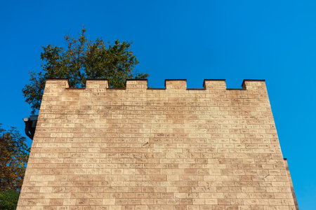 Brick wall of a building with decorative rectangular merlon. Yellow facade of a building without windows against a blue sky on a sunny dayの写真素材