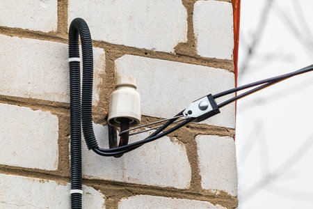 Fastening an electric wire with a tension clamp to a brick wall of a building facade. Corrugated wire and electric ceramic insulatorの写真素材