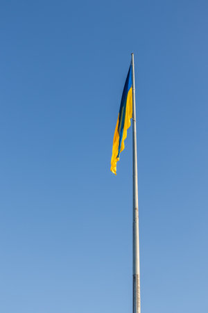 The flag of Ukraine on a high flagpole. The national Ukrainian flag against a clear blue sky. The flag does not flutter, there is no windの写真素材