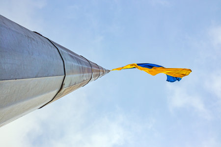 Flag of Ukraine on a high flagpole. Yellow and blue large national Ukrainian flag, blue sky in the daytime. View from belowの写真素材