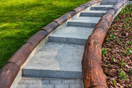 Modern stone staircase with wooden sides in the garden or park near the lawn and flowerbed. Stone and wood - materials for outdoor stairsの写真素材