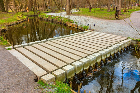 Modern low concrete bridge over a stream with water. Rectangular footbridge in a city garden or parkの写真素材