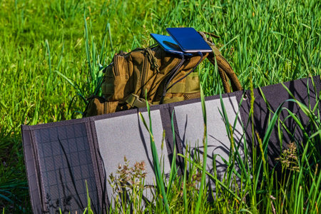 Portable solar panel folding on green grass near backpack. Solar power charging station for smartphones and personal devicesの写真素材