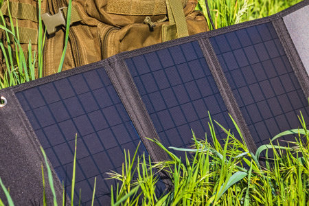 Solar panel foldable for hiking and travel. Portable solar power charging station near backpack on green grassの写真素材