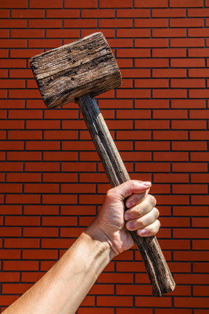 Large old wooden hammer in hand against brick wallの写真素材