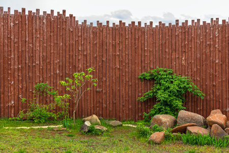 A tall wooden fence made of vertical logs and textured wood. Green grass and vegetation. No one, daytimeの写真素材