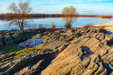 Rocky bank of Dnieper river. Landscape with granite stones and trees near water. Rock-register in Kremenchuk city, Ukraine. Dnipro river on a sunny dayの写真素材
