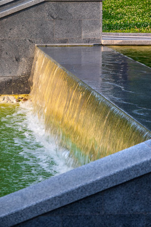 Waterfall in the park with a cascade of artificial decorative ponds framed by stone and granite slabs. Flowing water falls and foamの写真素材