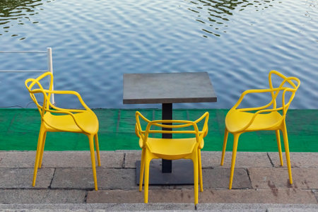 Table and yellow plastic chairs on the shore near the water. Empty cafe area on the embankmentの写真素材