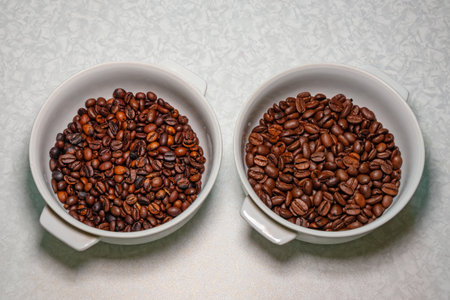 Comparison of roasted coffee beans in white plates on a table. Different sizes and qualities of whole coffee beansの写真素材