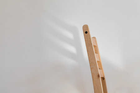 Chair dreaming of wings; the back of a wooden chair casts a wing-shaped shadow on a clean white wall behind itの写真素材