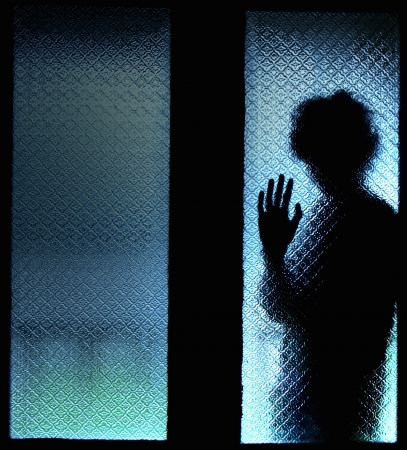 Scared boy behind glass door showing one handの写真素材