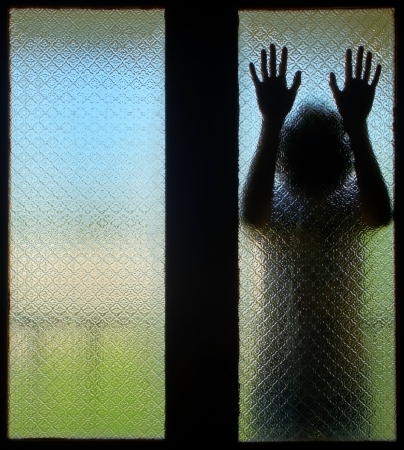 Scared boy behind glass door showing two handsの写真素材