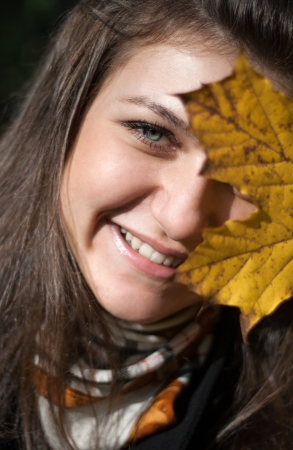 Smiling girl hiding her eye behind yellow leafの写真素材