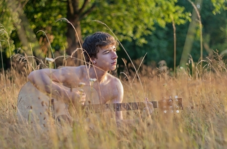 Teen with acoustic guitar in fieldの写真素材
