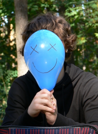 Boy hiding behind balloon with smileの写真素材
