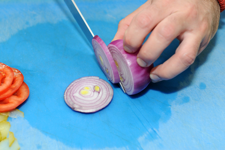 Chef chopping a red onion with a knife on the cutting boardの写真素材