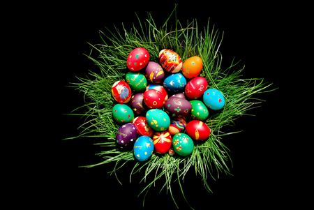 Several of colored Easter eggs lying in a bowl on a green grass, on a black backgroundの写真素材