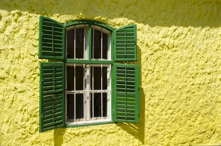 An old wooden window with metal bars on a yellow wall.の写真素材