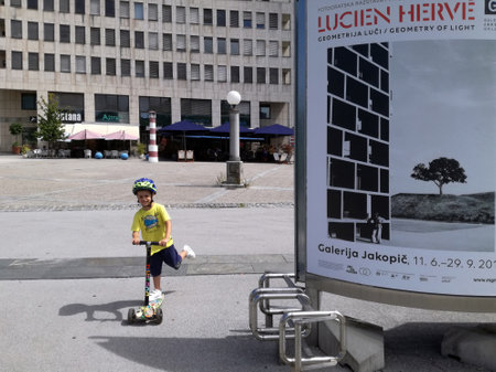 A boy with a scooter (trottinette) on the streets of Ljubljana, Slovenia - AUGUST 11, 2019Bulletin board for the exhibition of photographer Lucien Herve, Geometry of Light, at the Jakopic Gallery from June 11 to September 29, 2019のeditorial素材