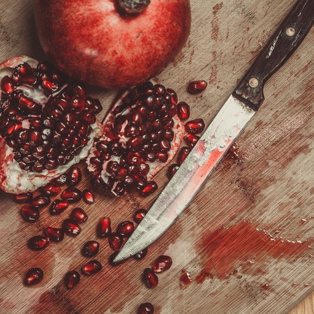 Chopped pomegranate with knife on wooden boardの写真素材