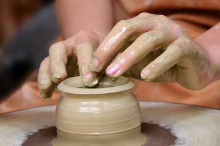 Clay pot on the wheel and two hands 