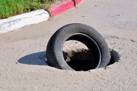 Automobile tyre in the open hatch of the well on the roadの写真素材