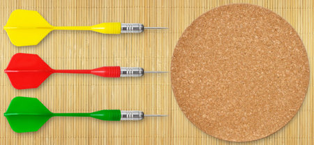 Three colored darts and a cork circle on the background of mat of bamboo