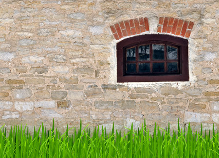 Old stone wall with a small window and a young grass in the backgroundの写真素材