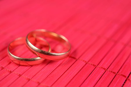 Two gold wedding rings on the red bamboo surfaceの写真素材