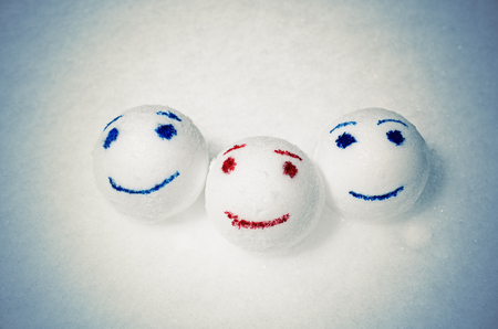 Three merry snowballs in the form of emoticons paint lie on the snow. Winter cold vintage toning. One snowball red, the other blue.の写真素材