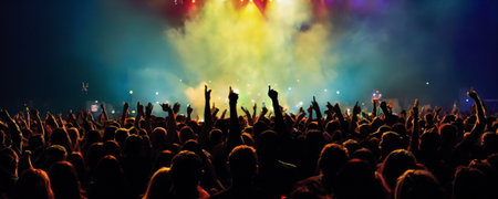 A lively crowd with raised hands enjoys a vibrant concert, illuminated by stunning stage lights under the evening skyの素材
