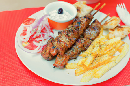 greek souvlaki with fries and cream cheese on a table in a restaurantの写真素材