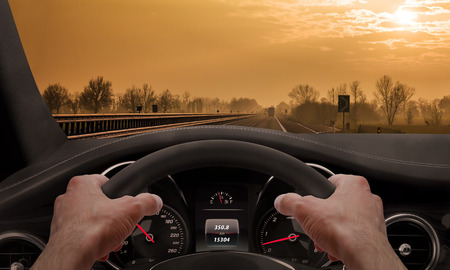 Driving at sunset. View from the driver angle while hands on the wheel.の写真素材