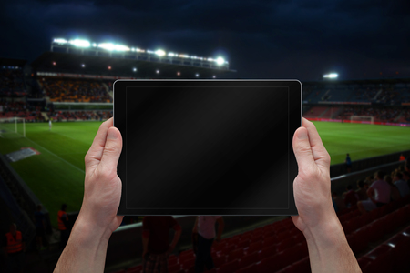 Man holding tablet with blank screen on soccer game. Stadium in background.の写真素材