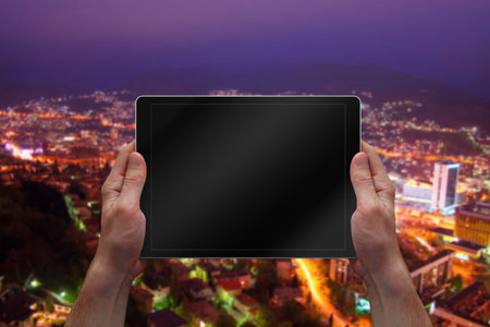 Man holding tablet with blank screen. City night landscape in background.